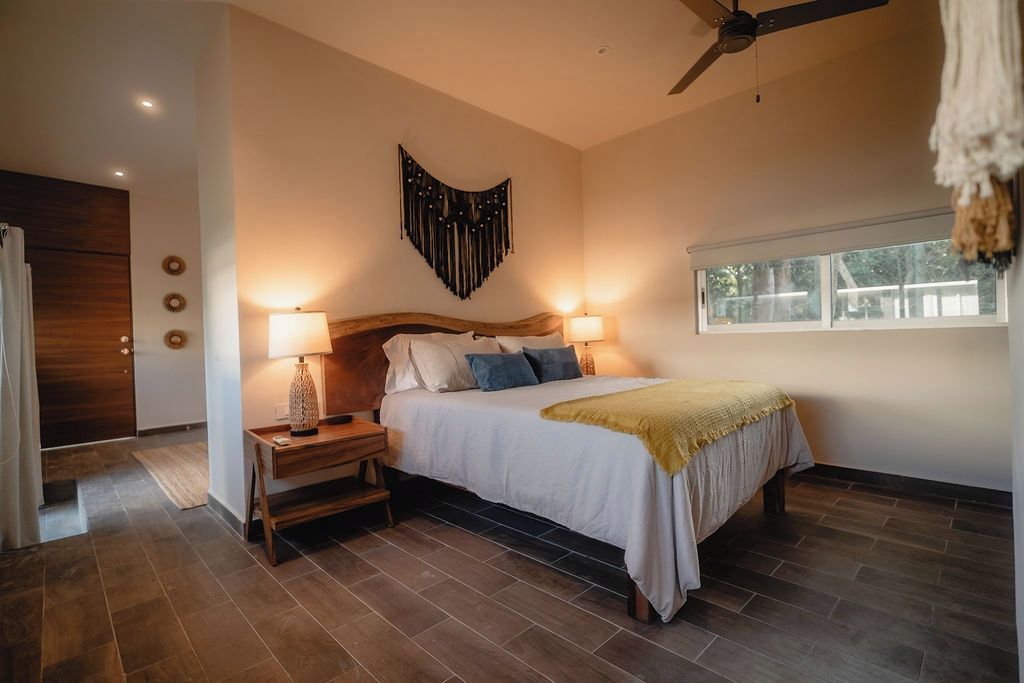 A bedroom with a bed, bedside lamps, a ceiling fan, a window, and a wall decoration.