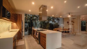 Une cuisine moderne dotée d’un îlot central, de meubles en bois et d’une grande fenêtre donnant sur un jardin.
