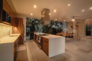 A modern kitchen with a central island, wooden cabinets, and a large window overlooking a garden.