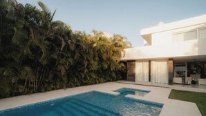 Une maison moderne dotée d’une piscine et bordée d’une haie verdoyante et luxuriante.