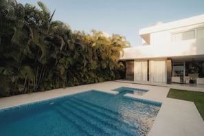 A modern house with a swimming pool and a lush green hedge.