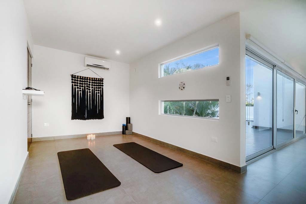 A spacious room with a large window, a yoga mat, and a wall-mounted air conditioner.
