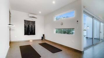 A spacious room with a large window, a yoga mat, and a wall-mounted air conditioner.