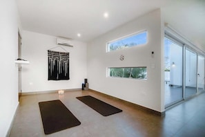 A spacious room with a large window, a yoga mat, and a wall-mounted air conditioner.