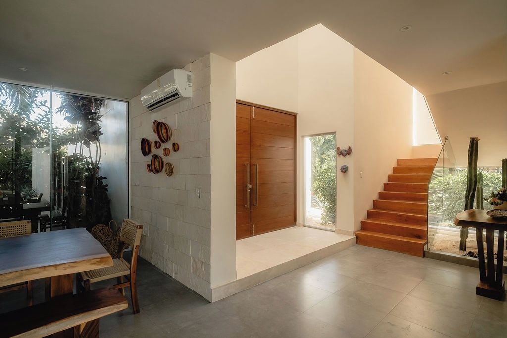 A modern interior with a dining area, a staircase, and a view of greenery outside.
