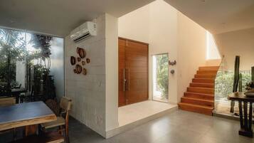 A modern interior with a dining area, a staircase, and a view of greenery outside.