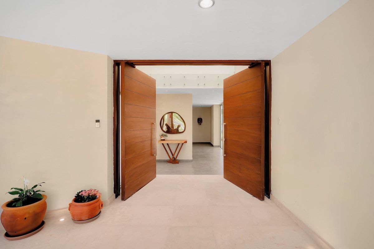 Un couloir avec des portes en bois, un miroir rond et deux plantes en pot.