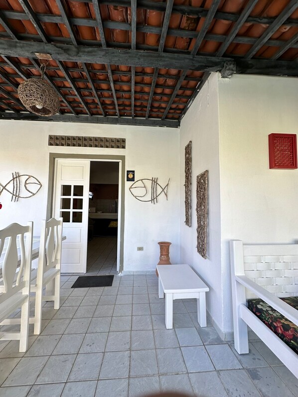 Quarto com piso ladrilhado, mobiliário branco, porta que dá para outro espaço e teto com padrão de grade.
