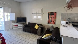 A living room with a sofa, a TV, a kitchen area with a microwave, and a tiled floor. - Bela Casa P Dos Carneiros cond.Beira Mar (Tamandaré)