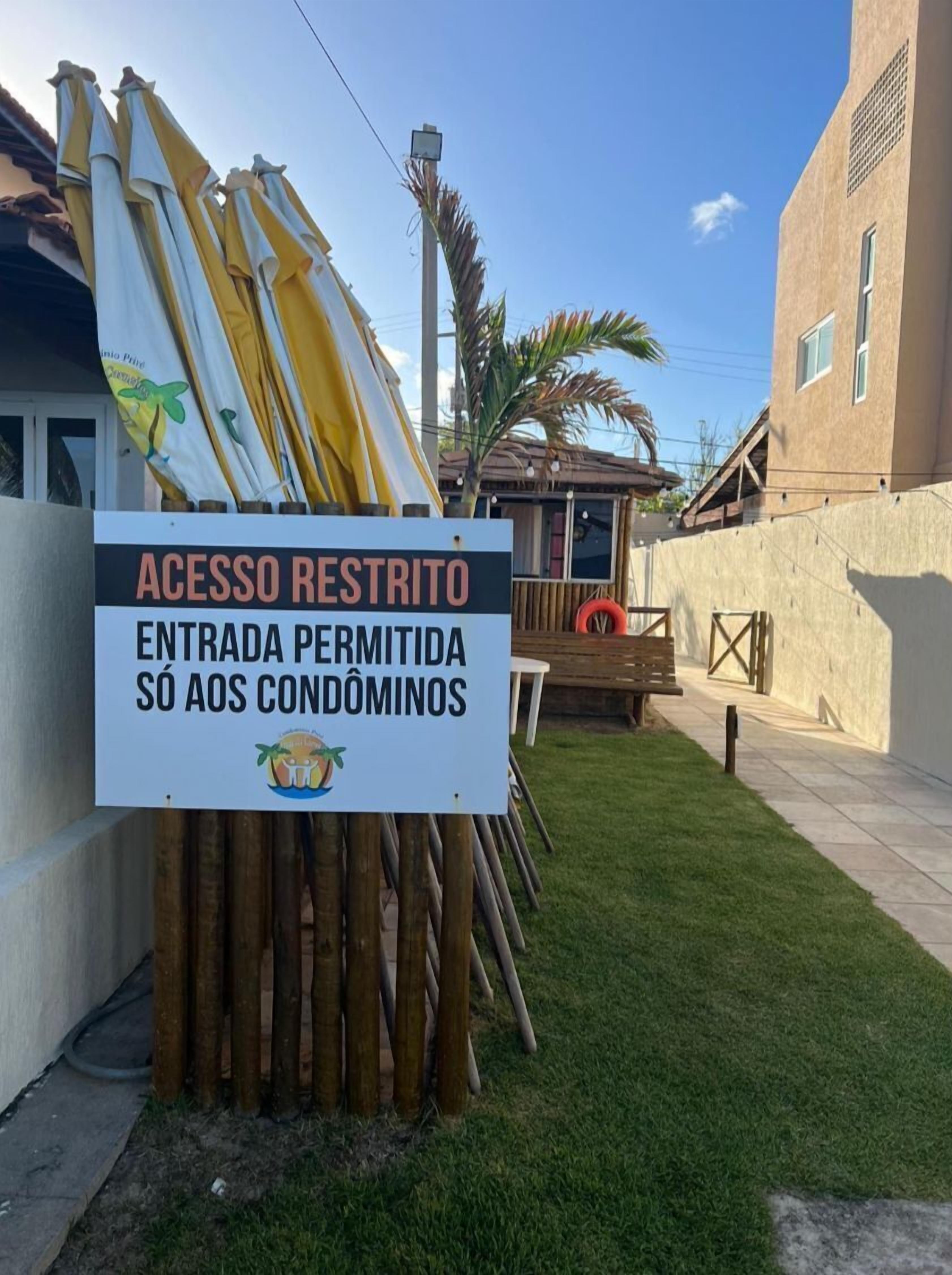 A sign indicating restricted access, with a wooden fence and umbrellas in the background.