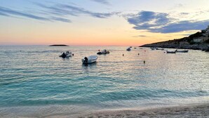 A coastal scene with boats on calm waters, a sandy beach, and a rocky cliff with buildings. - Apartment in Croatia Near Adriatic Coast (Vinodol)