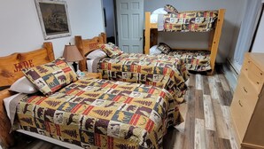 Une chambre avec deux lits en bois recouverts de couvertures colorées, une armoire en bois et un tableau encadré accroché au mur.