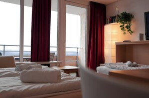 Quarto de hotel com cama, escrivaninha, cadeira e vista para o exterior.