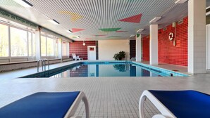 An indoor swimming pool with blue lounge chairs, a tiled floor, and a ceiling with colorful geometric patterns. - Appartement Peter in Freyung im Bayerischen Wald (Freyung)