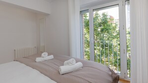 A bedroom with a large bed, a window with a view of trees, and a balcony.