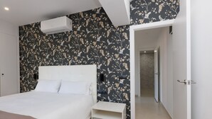 A bedroom with a bed, a nightstand, a wall-mounted air conditioner, and a door leading to another room.