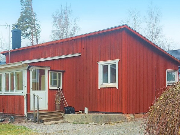 A red wooden house with a white door, a small porch, and a chimney.