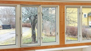 Een kamer met een groot raam, uitzicht op een tuin met een boom en een geel gebouw.