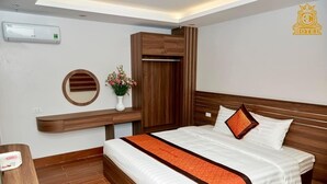 Une chambre d’hôtel avec un lit, une armoire en bois, un miroir et une petite table sur laquelle est posé un vase de fleurs.
