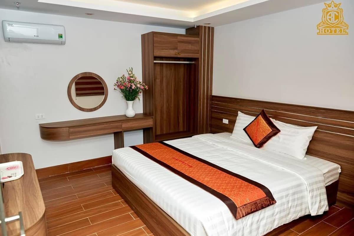 A hotel room with a bed, a wooden wardrobe, a mirror, and a small table with a vase of flowers.