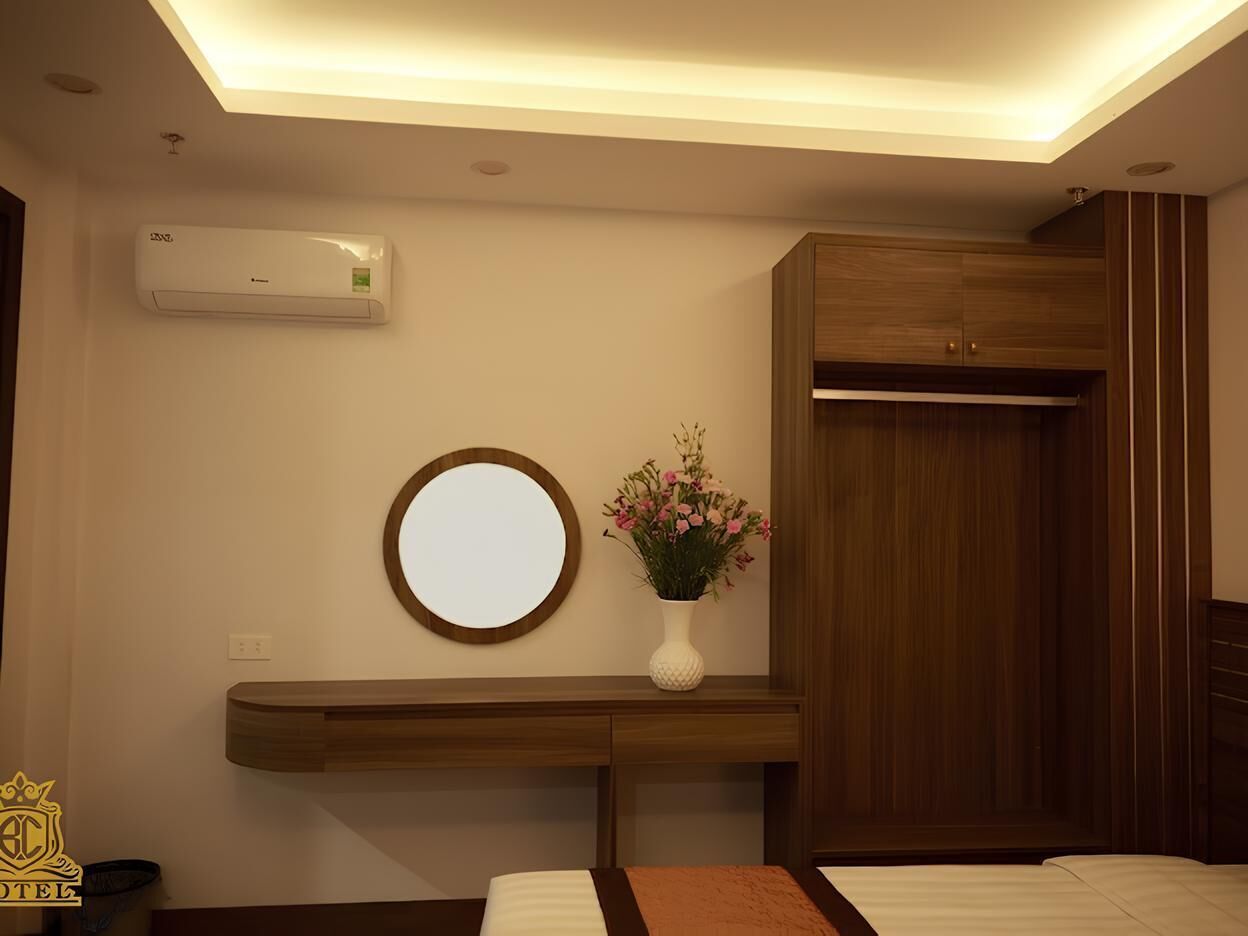 A hotel room with a wooden vanity, a round mirror, a vase with flowers, and a wardrobe.