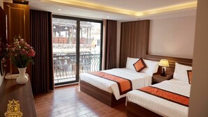 Une chambre d’hôtel avec deux lits, un balcon offrant une vue agréable et un bureau en bois agrémenté d’un vase de fleurs.