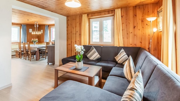 A modern living room with a sofa, coffee table, and a dining area with chairs and a table. - Holiday Home in the Silvretta-montafon ski Area (Sankt Gallenkirch)
