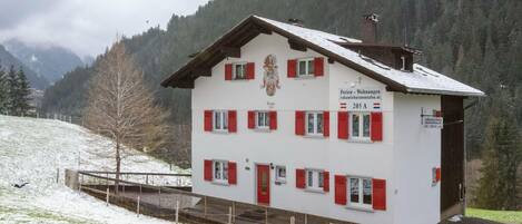 A two-story building with red shutters, a coat of arms, and a sign indicating it is a vacation rental.