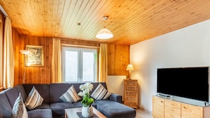 A cozy living room with a sectional sofa, a wooden coffee table, a TV on a wooden cabinet, and a window with curtains. - Holiday Home in the Silvretta-montafon ski Area (Sankt Gallenkirch)