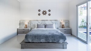 A modern bedroom with a large bed, marble headboard, two bedside tables with lamps, and a view of a swimming pool through a glass door.