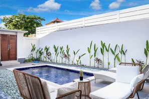 A swimming pool with lounge chairs and a wall decorated with plants. - Kakadu Villa by Betterplace (Kerobokan)
