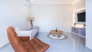 A modern living room with a sofa, a brown chair, a coffee table, and a TV on a stand.
