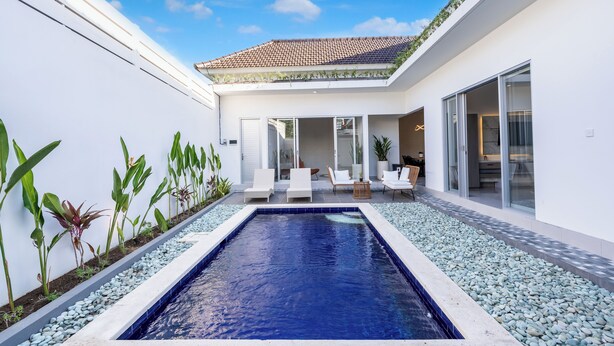 A modern outdoor pool area with a tiled roof, surrounded by white walls and plants.