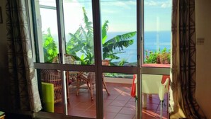 A room with a large sliding glass door leading to a balcony with a view of the ocean and tropical plants. - Holiday Home Casa Brisa Mar in Prazeres (Calheta)