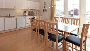 Une cuisine moderne avec des meubles blancs, une table à manger en bois avec six chaises et une grande fenêtre avec des rideaux.