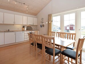 Una cocina moderna con armarios blancos, una mesa de comedor de madera con seis sillas y un amplio ventanal con cortinas.