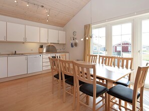 Una cocina moderna con armarios blancos, una mesa de comedor de madera con seis sillas y un amplio ventanal con cortinas.