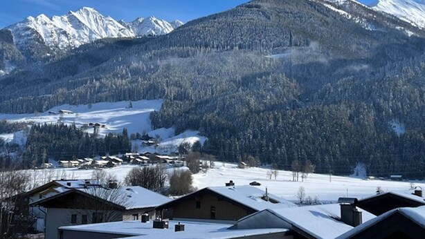 Eine Berglandschaft mit schneebedeckten Gipfeln und einem Tal mit Häusern.
