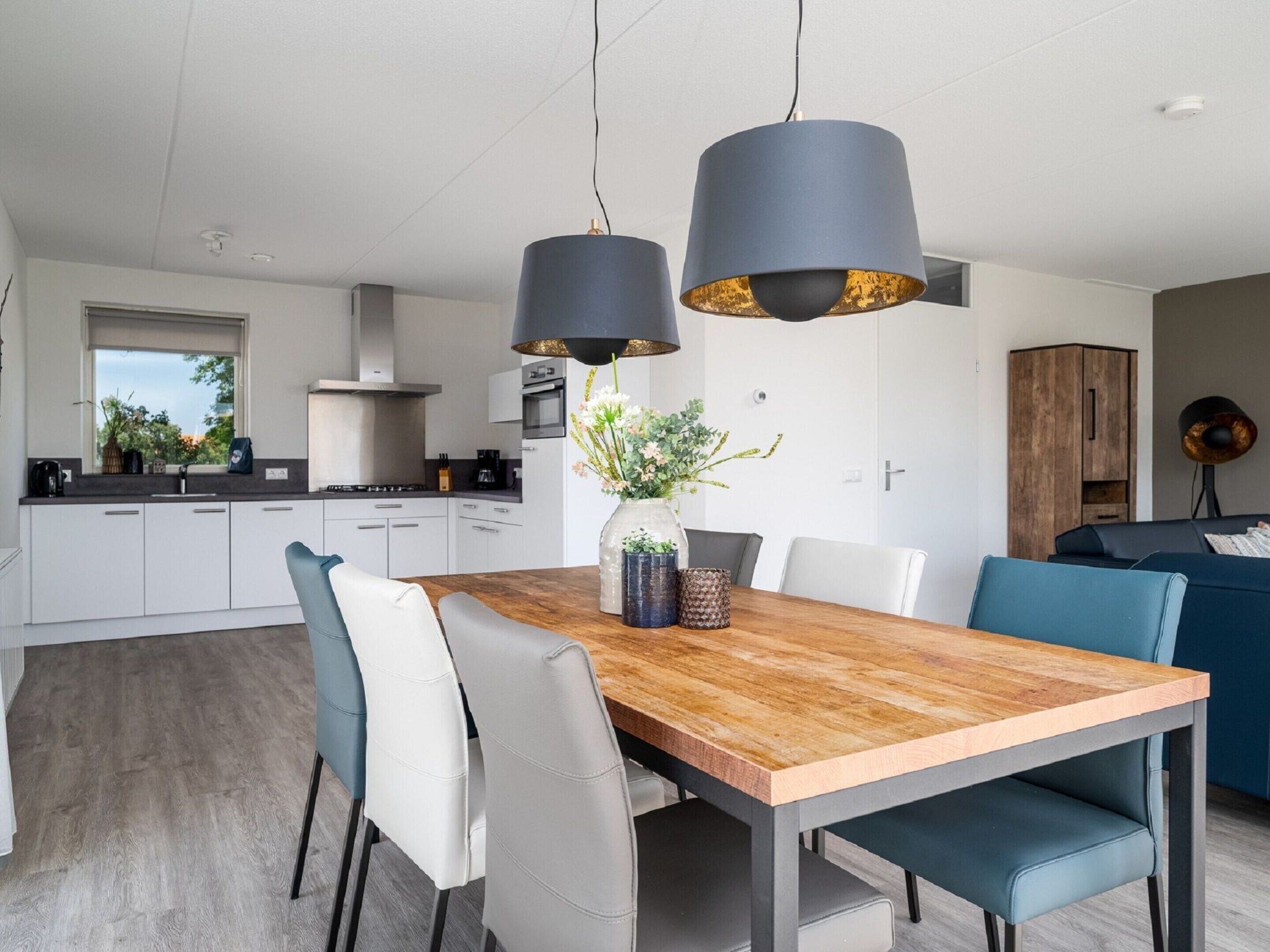 A modern kitchen with white cabinets, a wooden dining table, and two pendant lights.