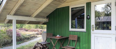 A covered outdoor seating area with a table and two chairs, a green wall, and a white door.