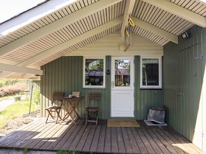 A covered porch with a table and chairs, a door, and windows.