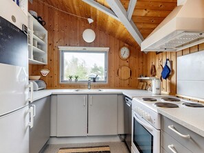 A kitchen with wooden walls, a window, a sink, cabinets, a stove, and a clock.