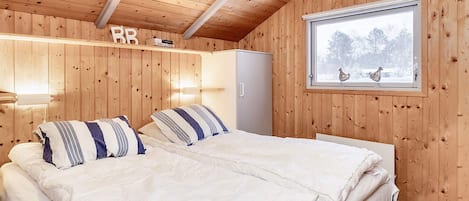 A wooden-paneled room with a bed, a window with a view of trees, and a shelf with books.