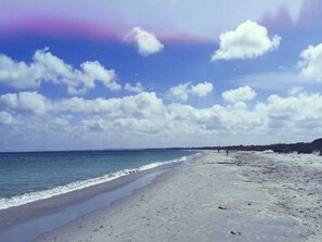 Une plage avec un ciel dégagé, une mer calme et une cÎte lointaine.