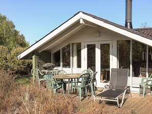 Ein überdachter Essbereich im Freien mit Tisch, Stühlen, einem Grill und Blick auf die umliegende Landschaft.