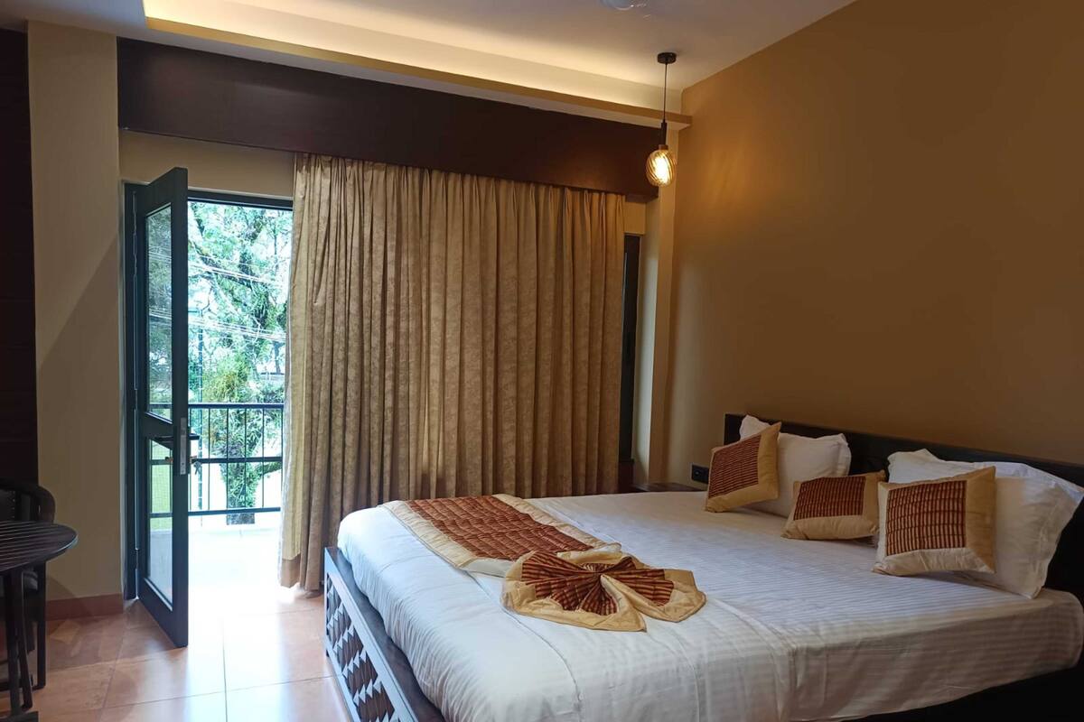 A hotel room with a large bed, a balcony with curtains, and a dining area.