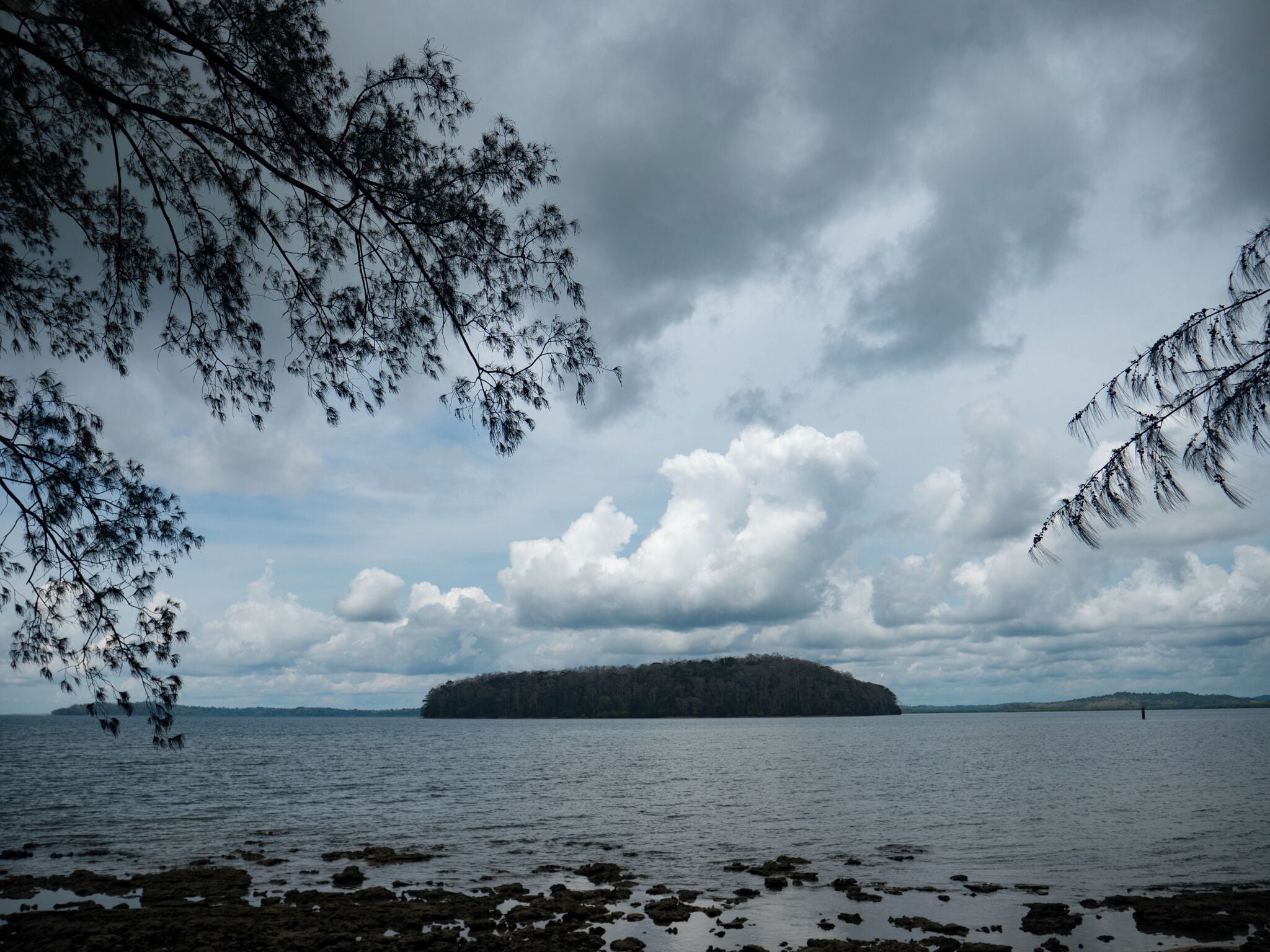 Un paysage côtier avec une petite île à l’horizon, entourée d’eau et sous un ciel nuageux.