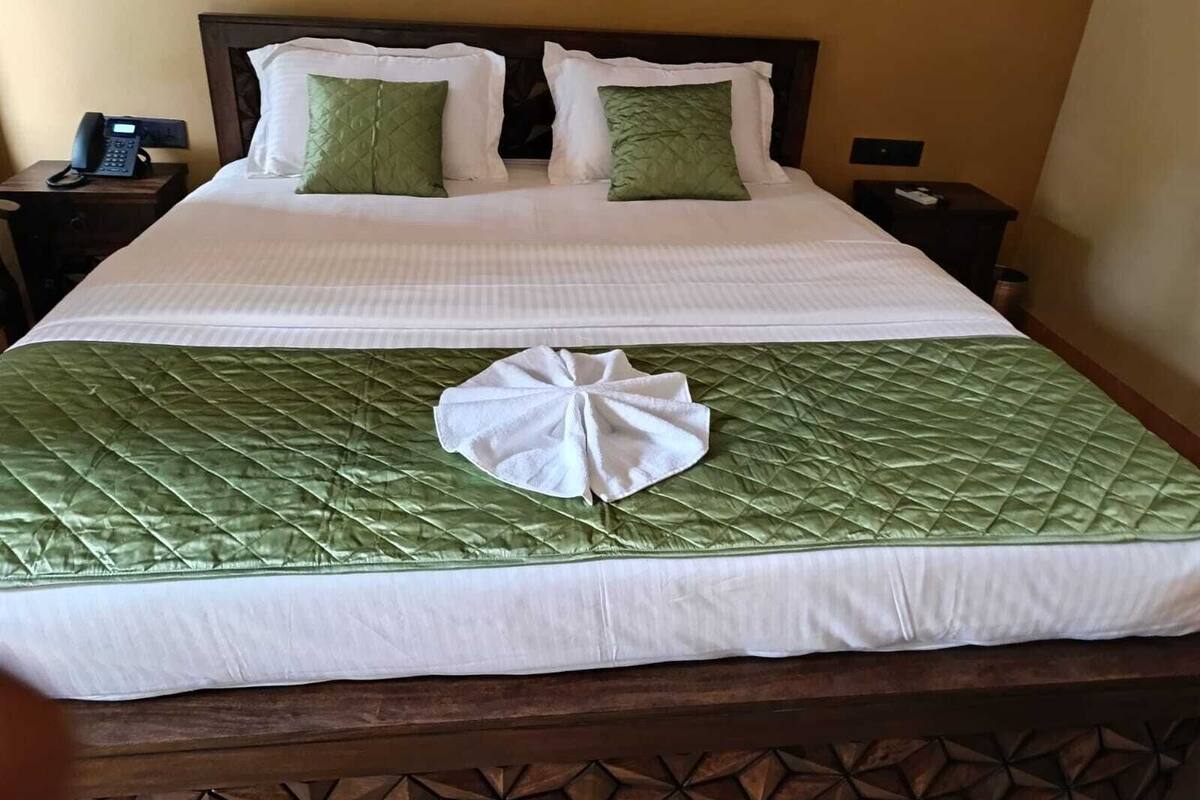 A neatly made bed with a green quilt and white linens, two green pillows, and a white towel on the bed.