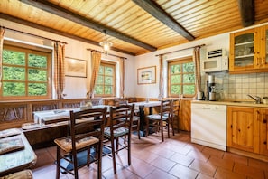 A rustic kitchen with wooden cabinets, a built-in dishwasher, and large windows with curtains.