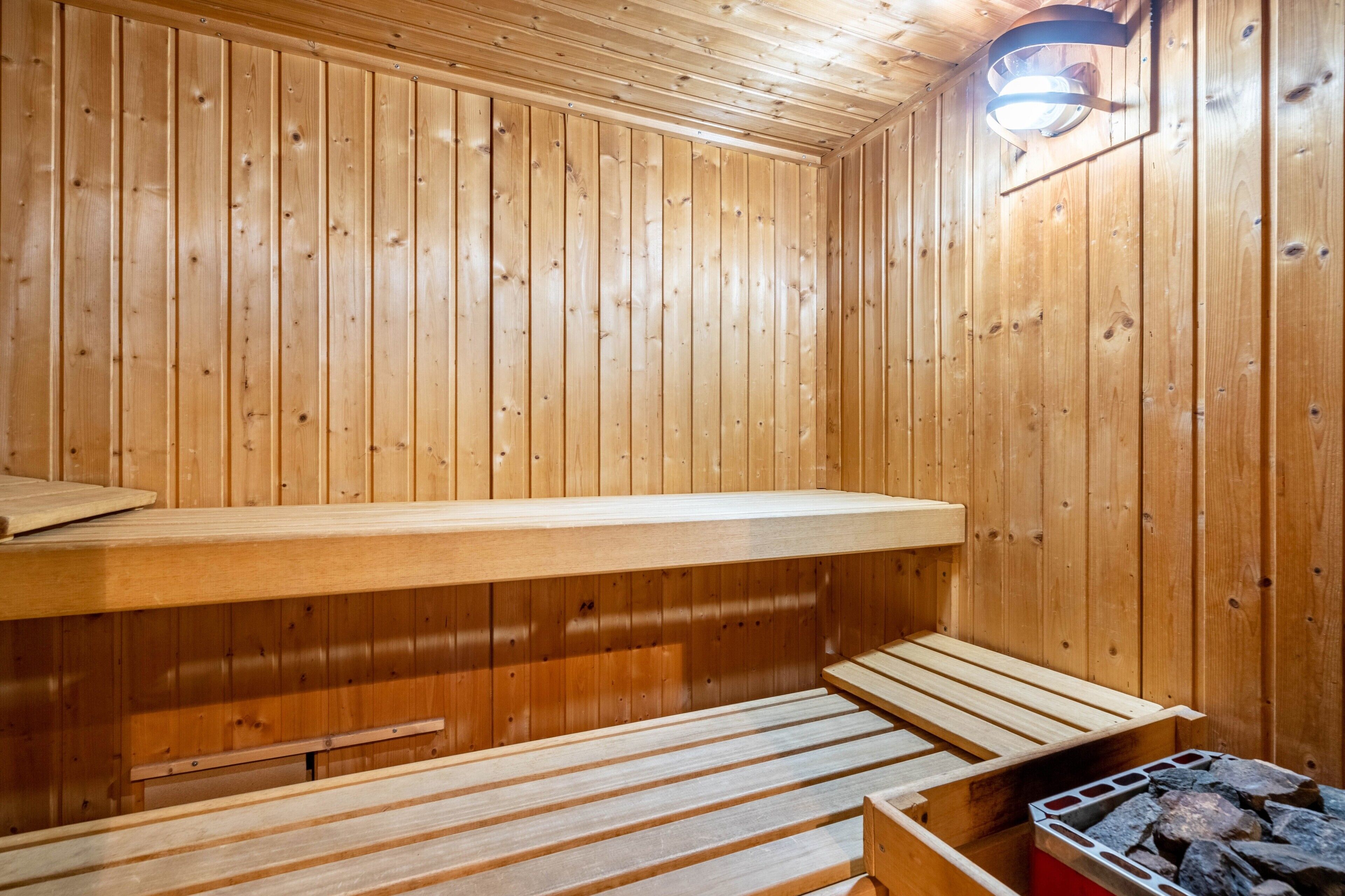 Un sauna en bois avec des bancs et un banc fixé au mur, ainsi qu’un tas de pierres dans un coin.
